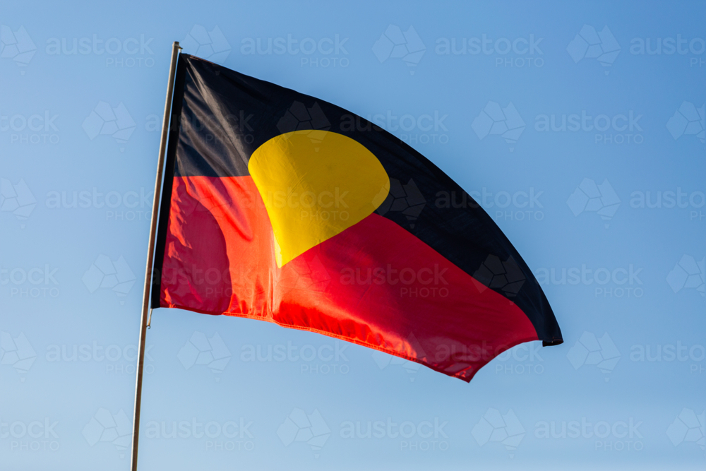 Black yellow and red First Nations Australian flag flying in blue sky - Australian Stock Image