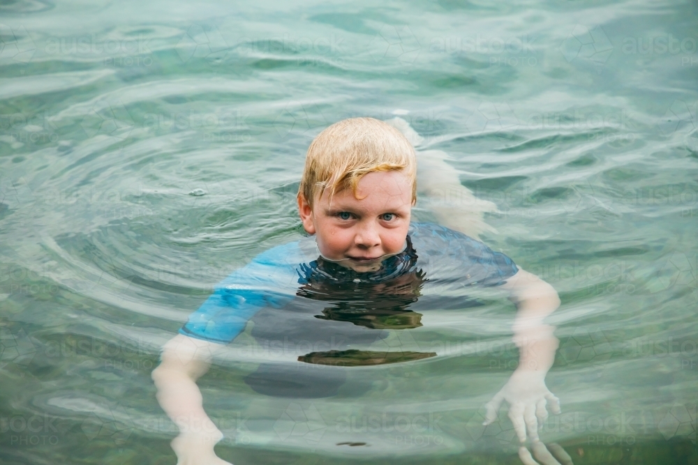 Blonde boy swimming with head just above water in clear saltwater pool on holiday in Newcastle - Australian Stock Image