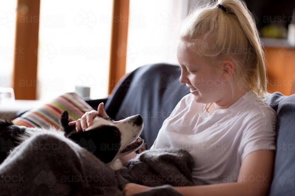 Blonde girl cuddling dog on couch - Australian Stock Image