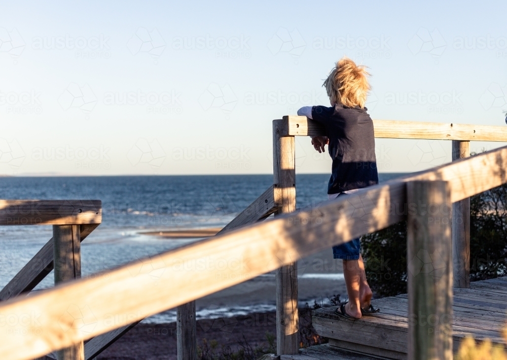 Blonde hair boy on boardwalk looking towards ocean - Australian Stock Image