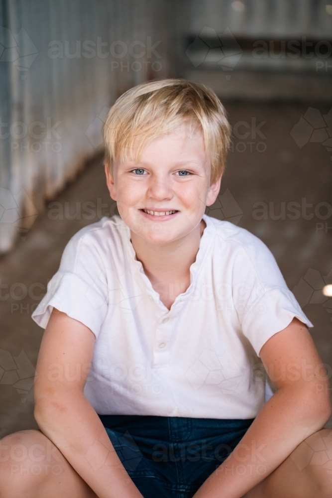 blonde pre-teen boy with relaxed pose sitting in rustic outdoor county setting - Australian Stock Image