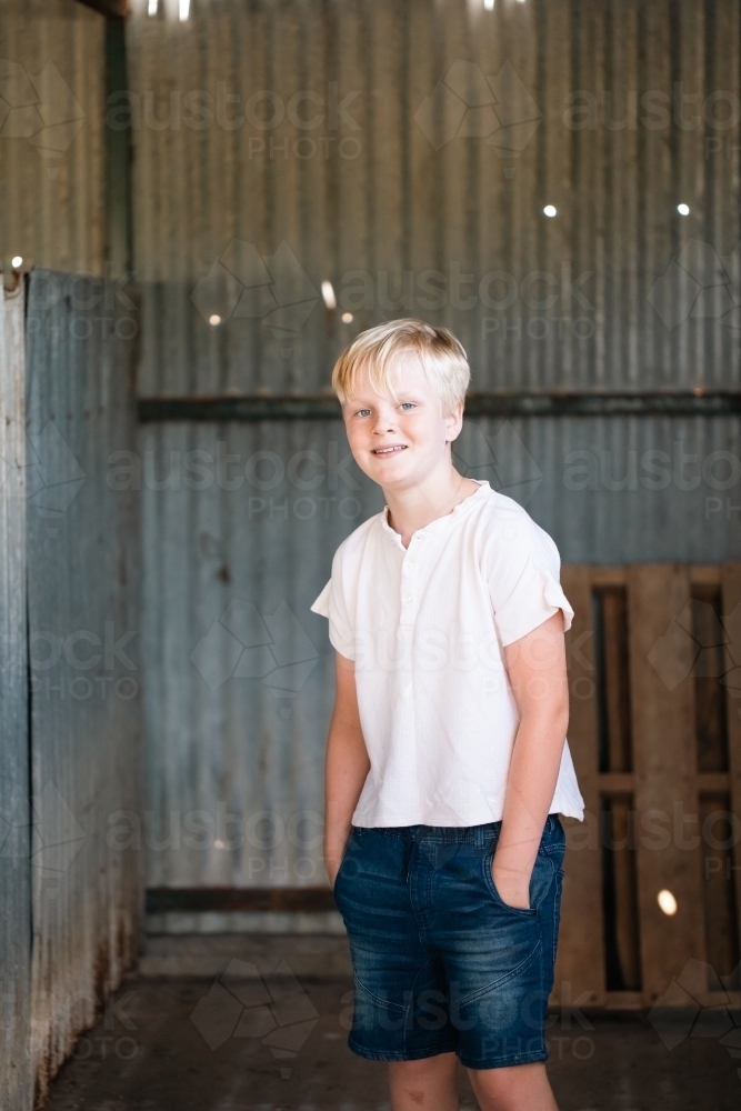 blonde pre-teen boy with relaxed pose standing in rustic county setting - Australian Stock Image