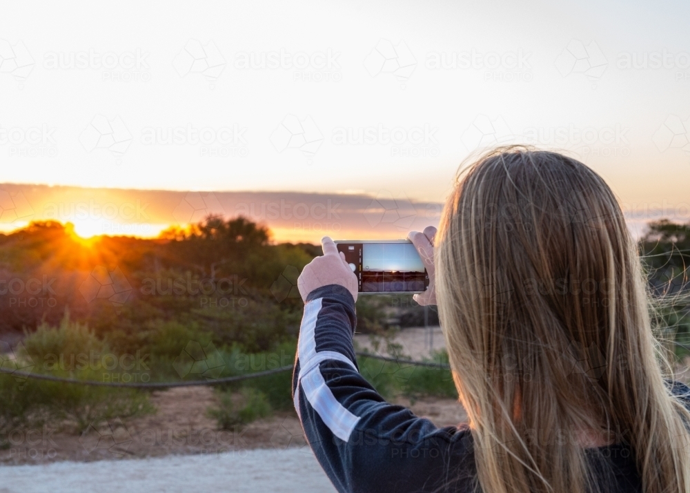 Blonde Teen Girl Taking Sunset Photo on Smart Phone - Australian Stock Image