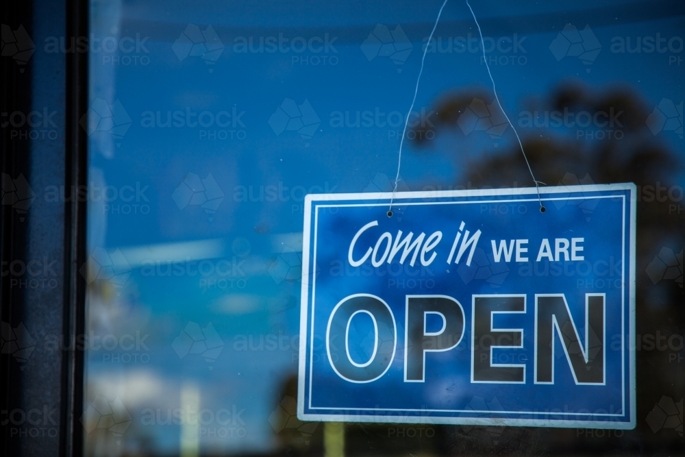 Blue come in we are open sign on glass shop door - Australian Stock Image