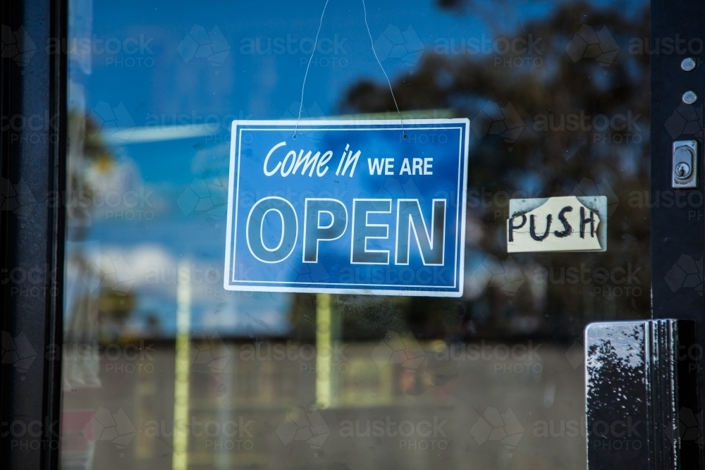 Blue come in we are open sign on glass shop door - Australian Stock Image