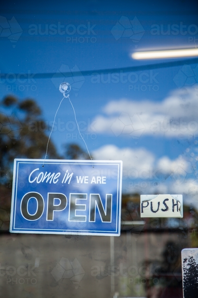 Blue come in we are open sign on glass shop door - Australian Stock Image