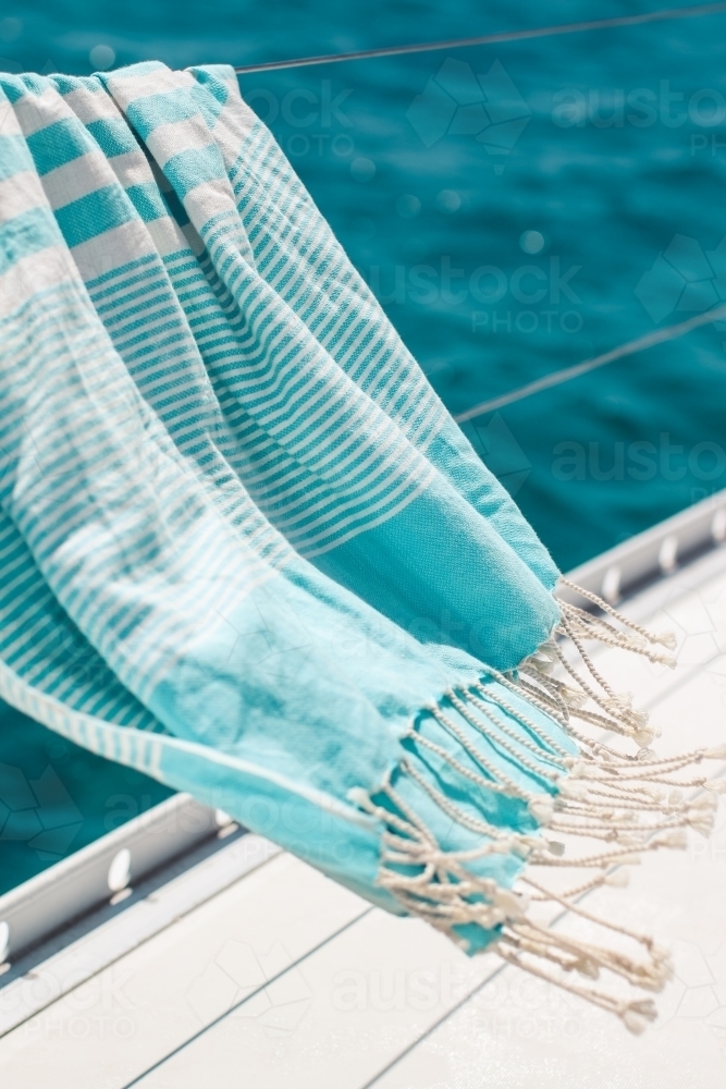 Blue turkish towel blowing on wire railing of boat on the water - Australian Stock Image