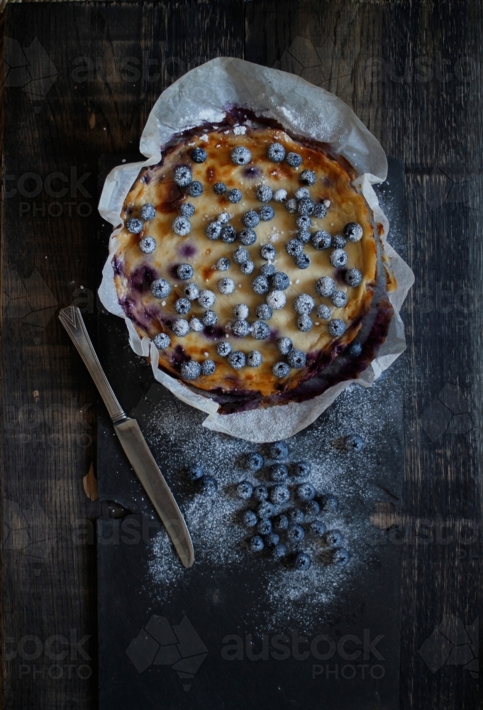 Blueberry cheesecake in baking paper on black background - Australian Stock Image