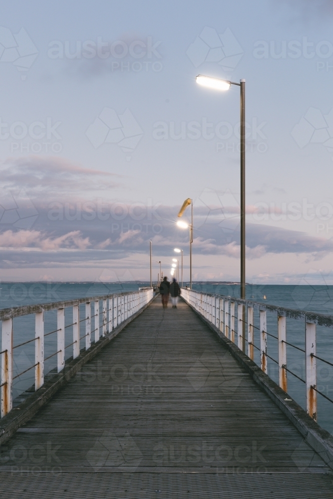 Blurred figures walking down the jetty in evening light - Australian Stock Image