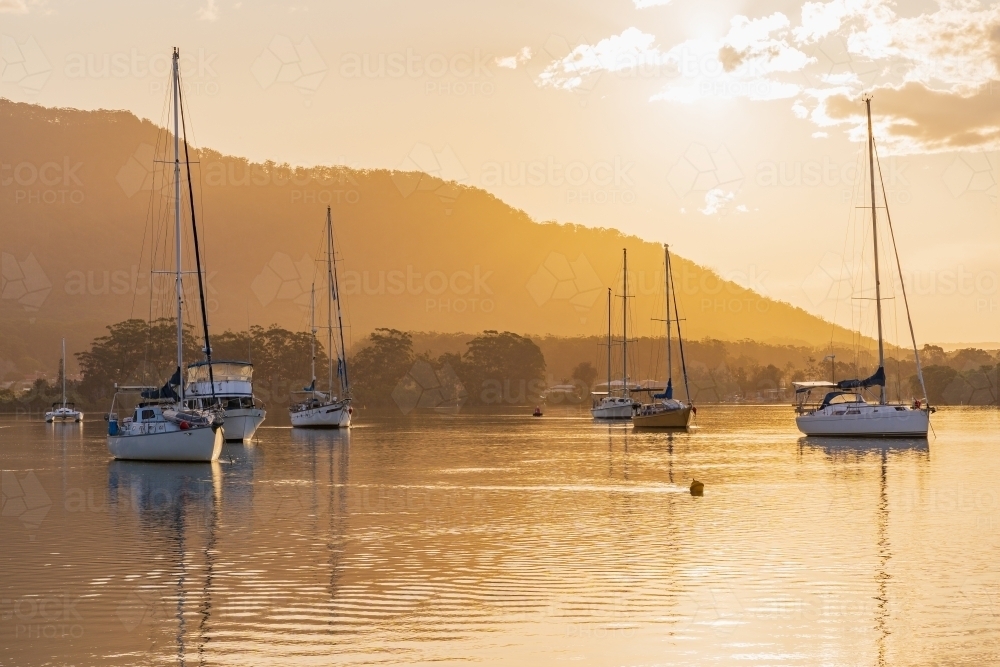 Boats and yachts moored on a still river in front of golden sunset - Australian Stock Image