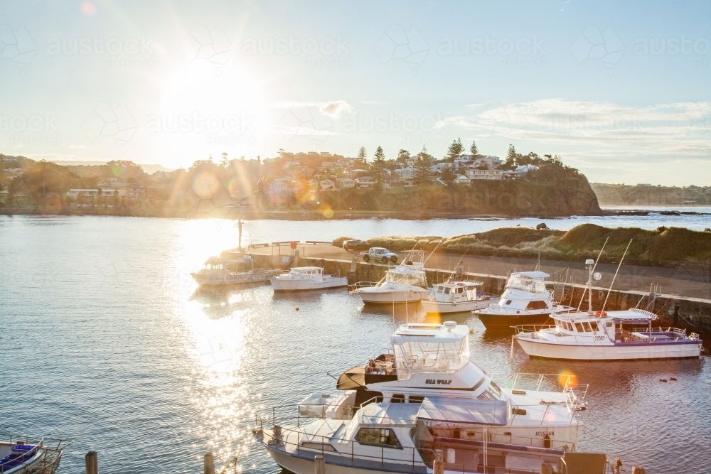 Boats docked in a harbour in Kiama with lens flare at sunset - Australian Stock Image