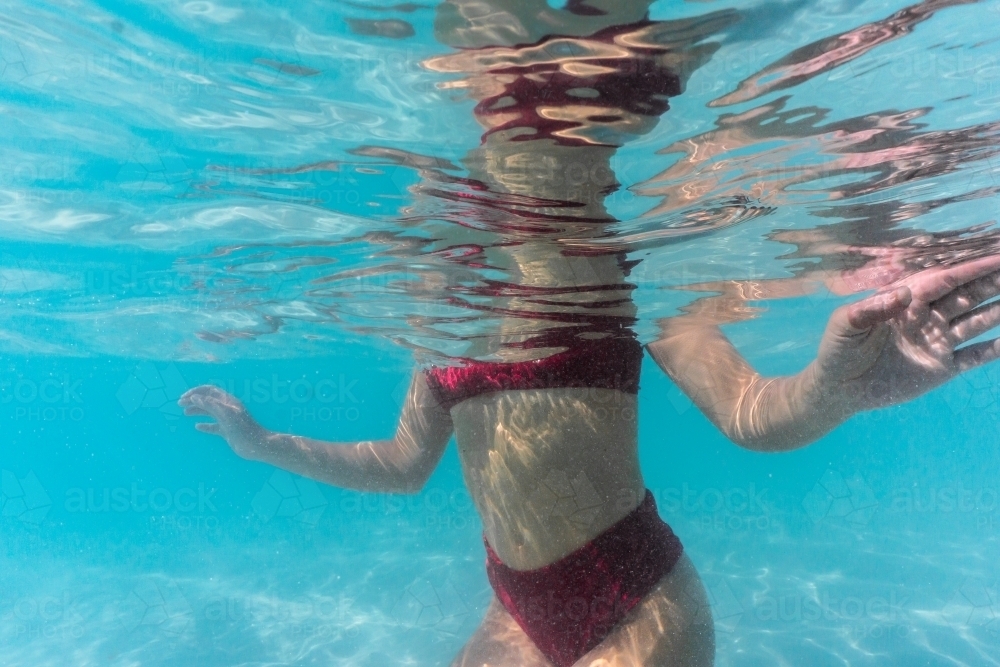 Body of woman in red bikini kneeling underwater in peaceful position with arms stretched out - Australian Stock Image