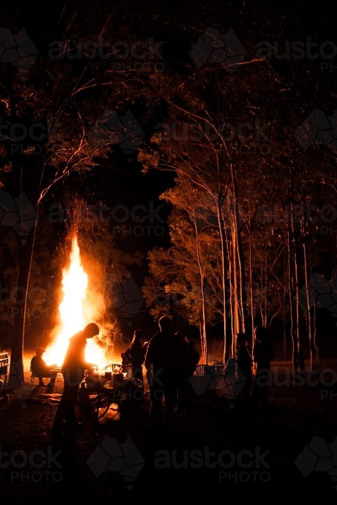 Bonfire blazing and silhouetted people eating together at night - Australian Stock Image