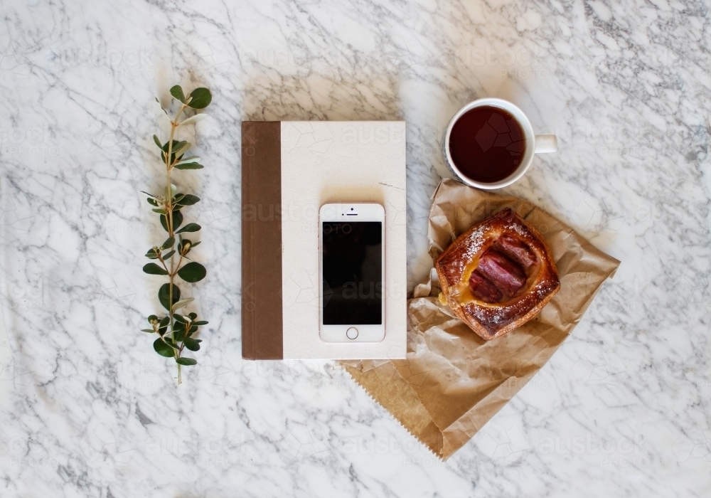 Book, iphone, coffee, pastry on marble coffee table - Australian Stock Image