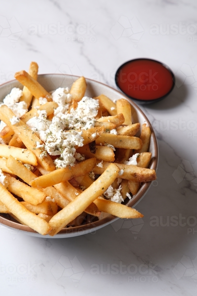 Bowl of hot chips with sprinkled feta cheese and side of tomato sauce - Australian Stock Image