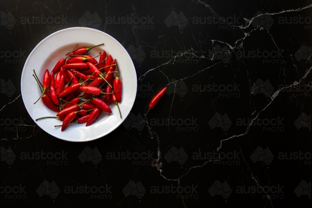 bowl of red chillies on black background - Australian Stock Image