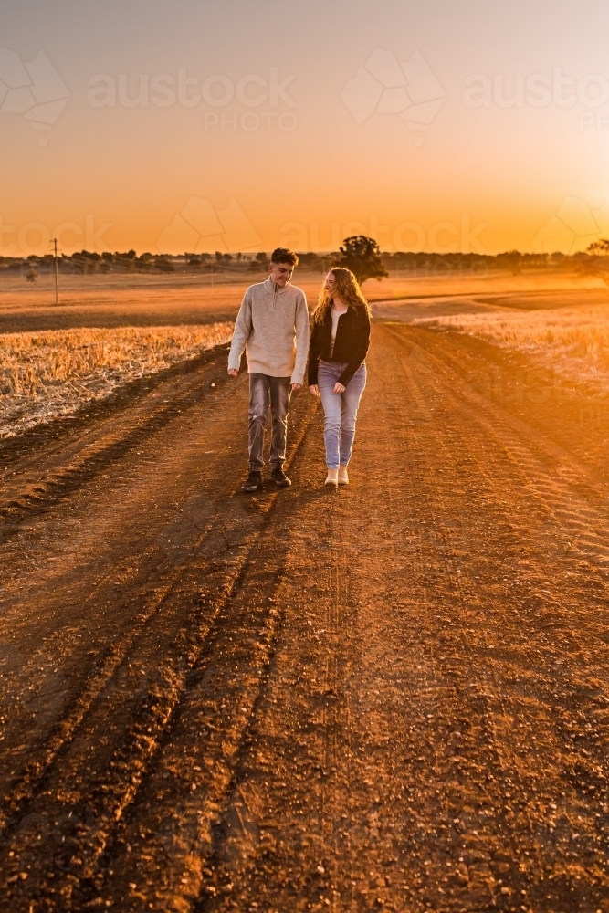 Boy and girl walking together on rural dirt road at sunset - Australian Stock Image
