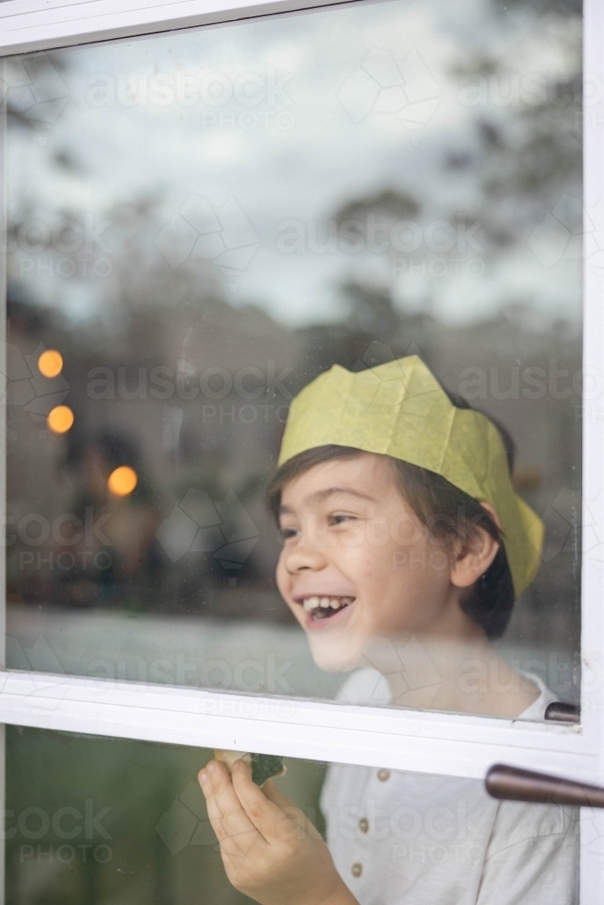 Boy at window wearing a Christmas crown and eating a mince pie - Australian Stock Image