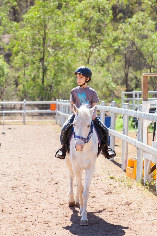 Boy child riding white pony during lesson - Australian Stock Image