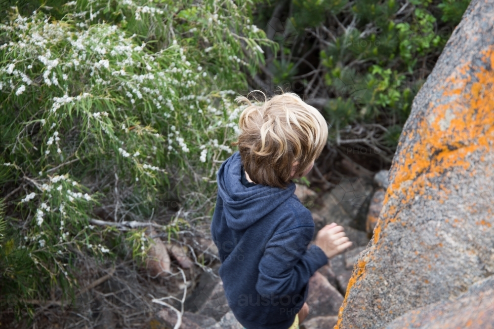 Boy climbing down rocks in bushland - Australian Stock Image