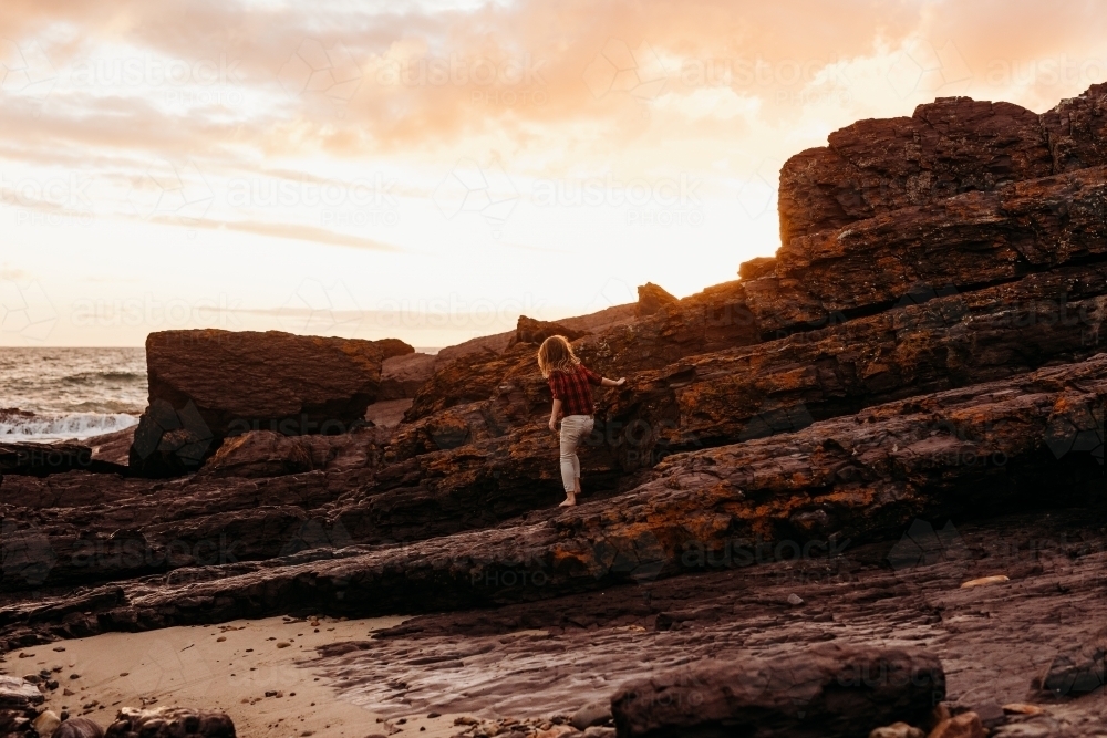 Boy climbing on rocks at sunset - Australian Stock Image