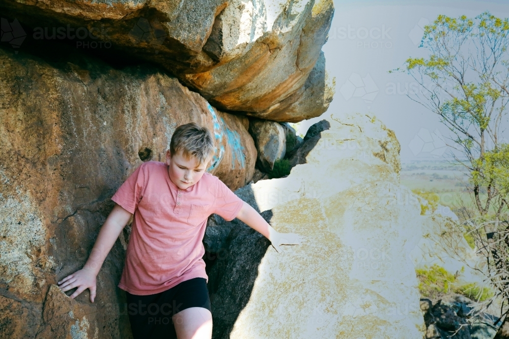 Boy climbing through rocks at on side of hill - Australian Stock Image
