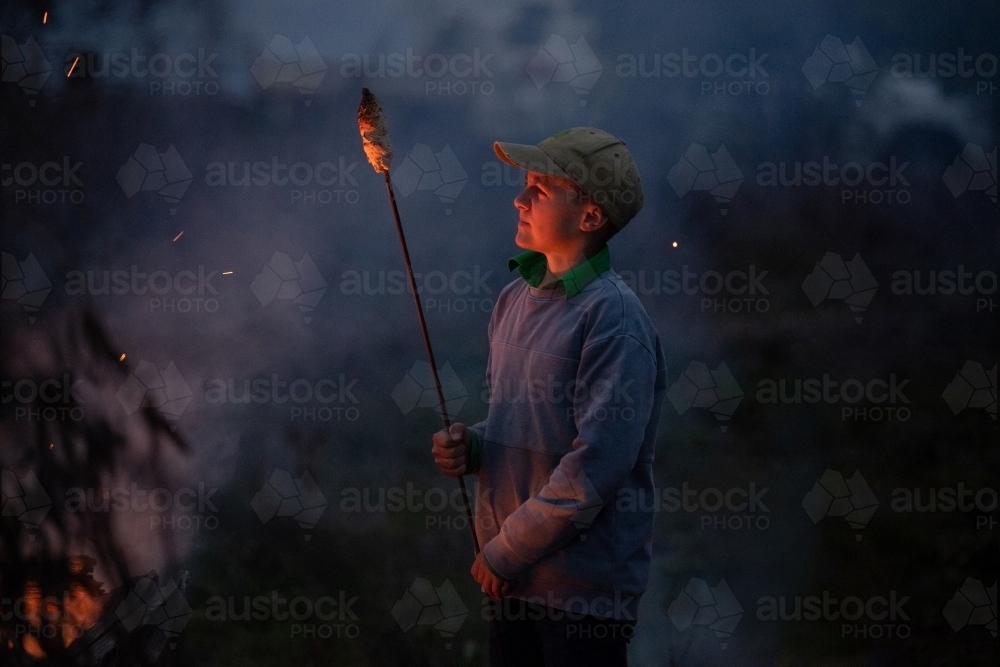 Boy cooks damper on bonfire - Australian Stock Image