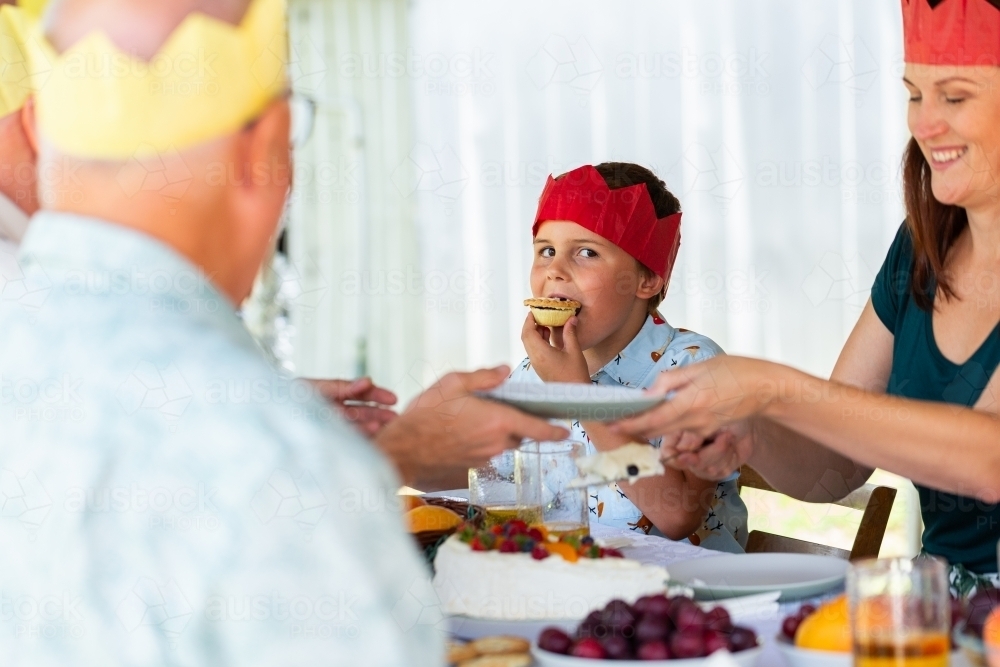 boy eating fruit mince pie while family is distracted serving up dessert - Australian Stock Image