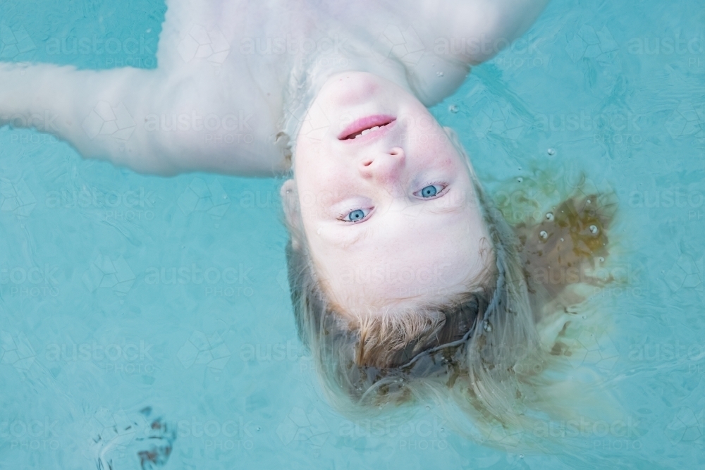 Boy floating upside down in resort swimming pool, close up of face - Australian Stock Image