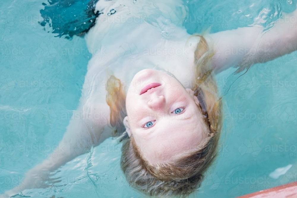 Boy floating upside down in resort swimming pool, close up of face - Australian Stock Image