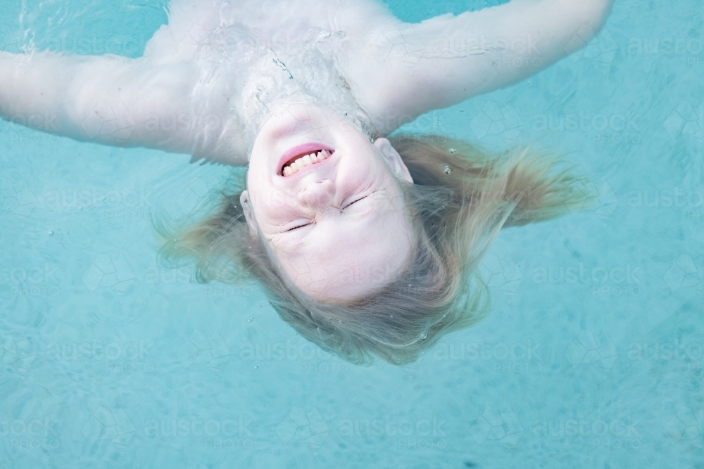 Boy floating upside down vibrant blue swimming pool with face scrunched up - Australian Stock Image