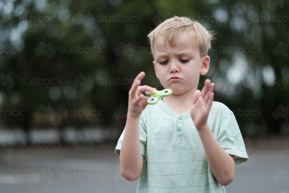 Boy frowning playing with fidget spinner toy - Australian Stock Image