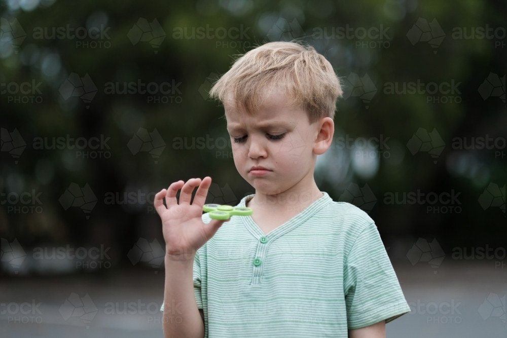 Boy frowning playing with fidget spinner toy - Australian Stock Image