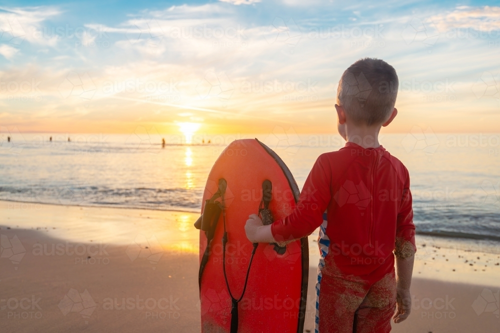 Boy holding bodyboard whilst standing at the beach and watching sunset, Chrieties Beach, SA - Australian Stock Image