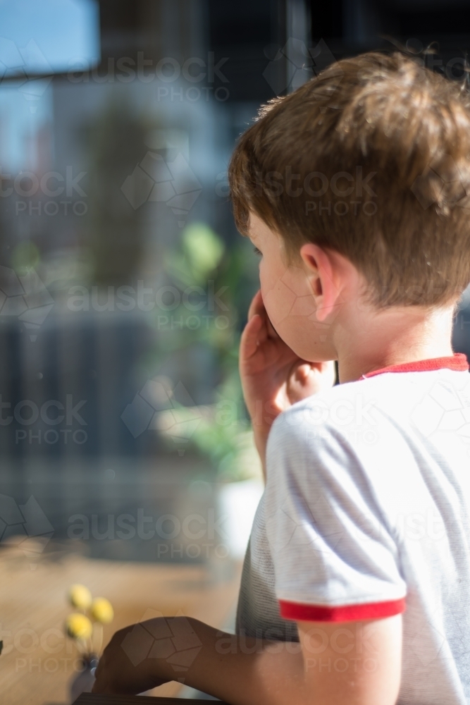 Boy holding his mouth looking off into distance - Australian Stock Image