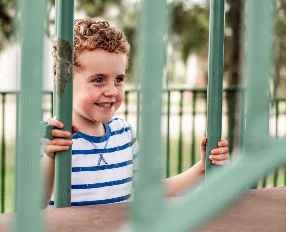 Boy holding onto bars of climbing area at park - Australian Stock Image