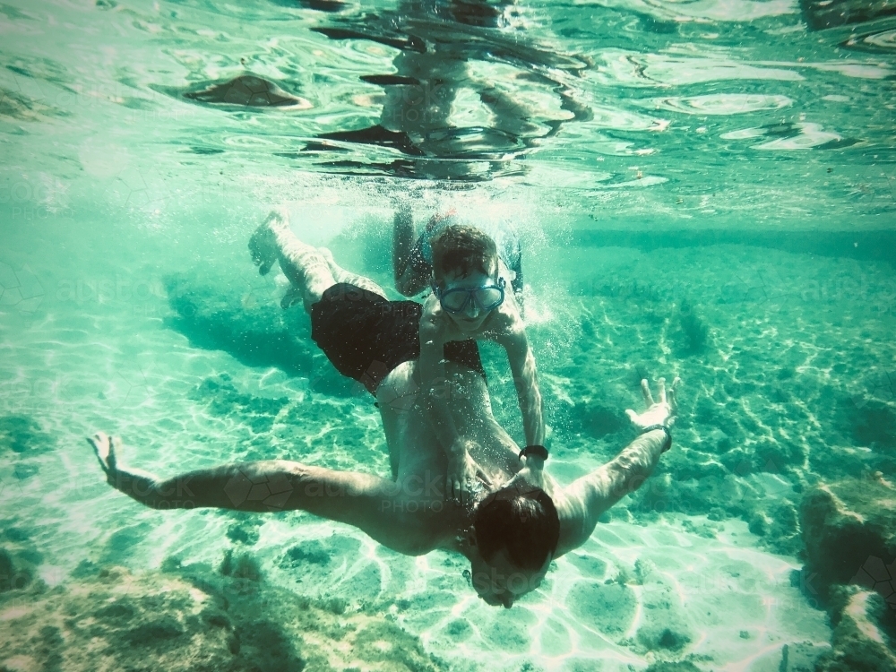 boy holding onto man diving underwater, taken underwater - Australian Stock Image