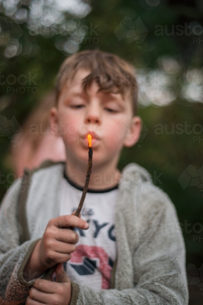 Boy in nature blowing a stick lit by fire - Australian Stock Image