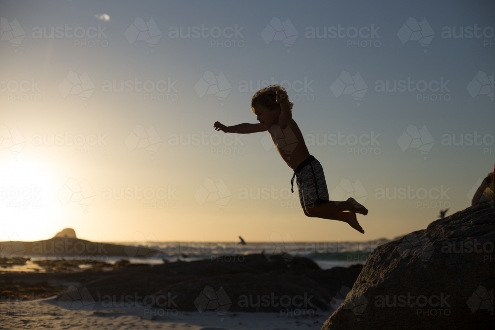 Boy jumping off a rock on the beach - Australian Stock Image