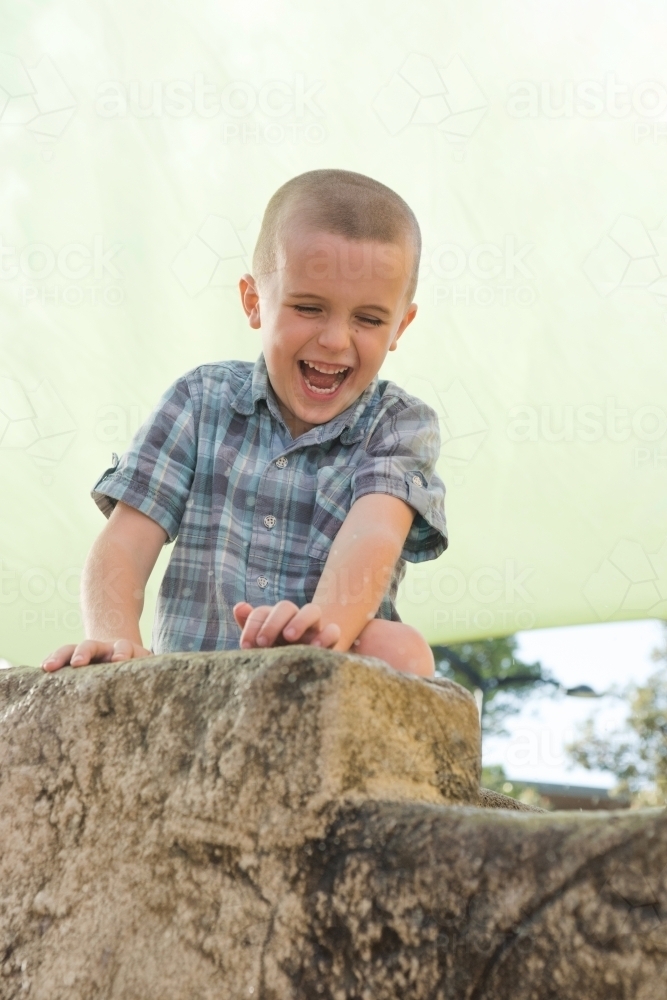 Boy laughing at park while standing in front of play equipment. - Australian Stock Image