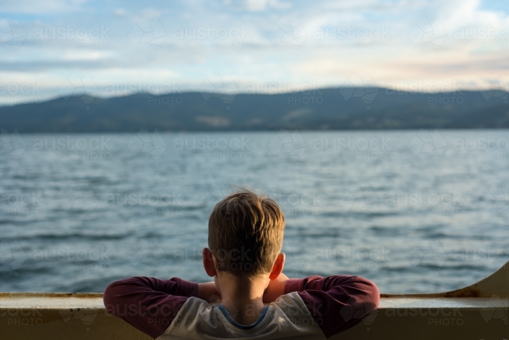 Boy looking above railling on ferry at the ocean - Australian Stock Image