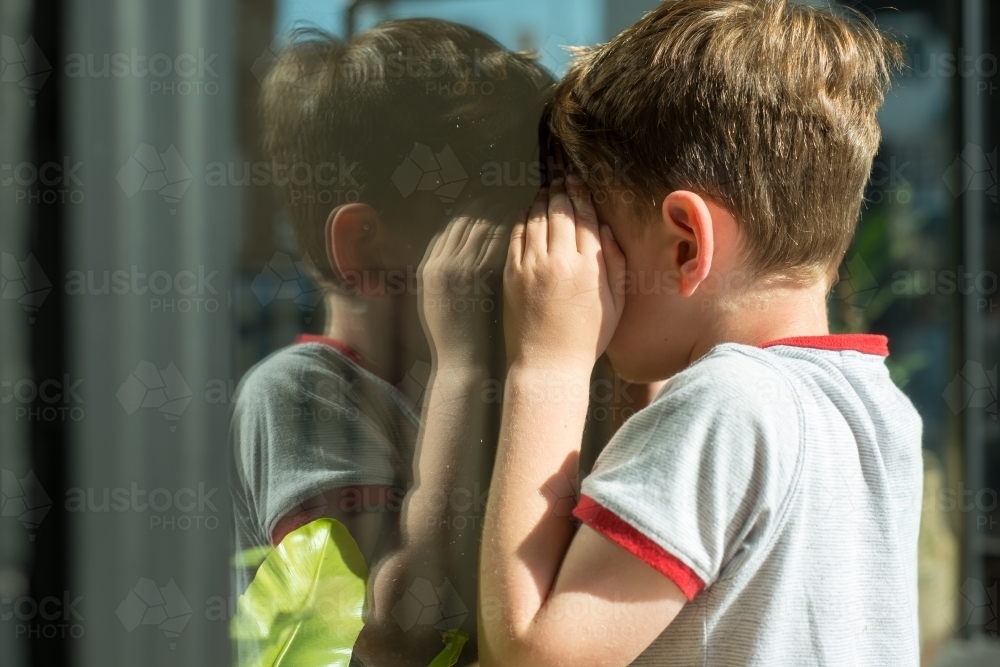 Boy looking into window with reflections - Australian Stock Image