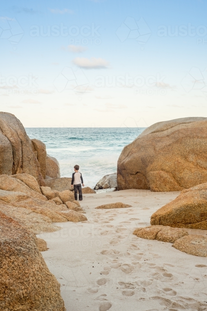 Boy on sandy beach surrounded by boulder rocks - Australian Stock Image