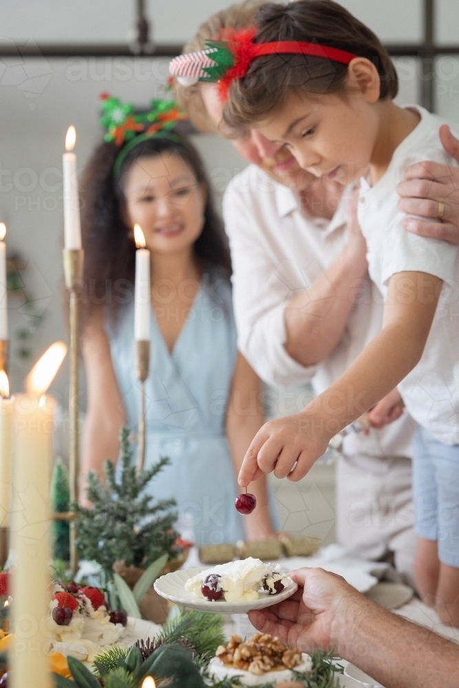 Boy placing cherry with help of parents - Australian Stock Image