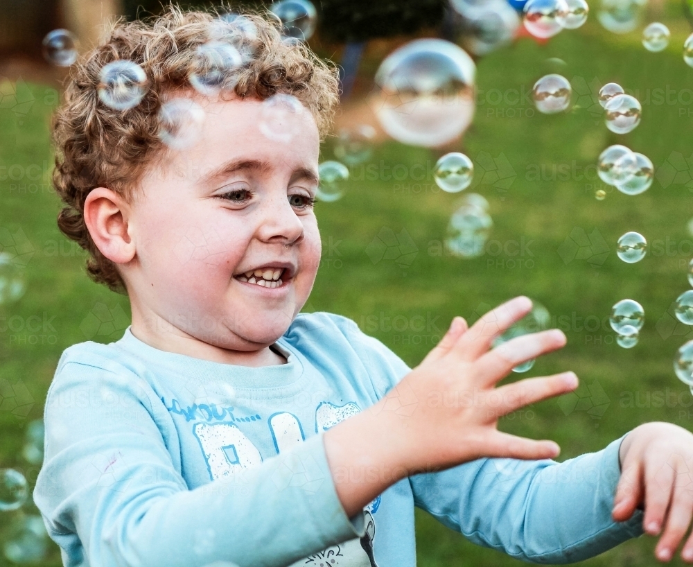 Boy playing in backyard with bubbles - Australian Stock Image