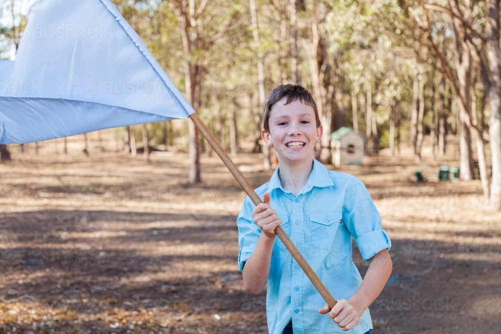 Boy playing with light blue flag in backyard - Australian Stock Image