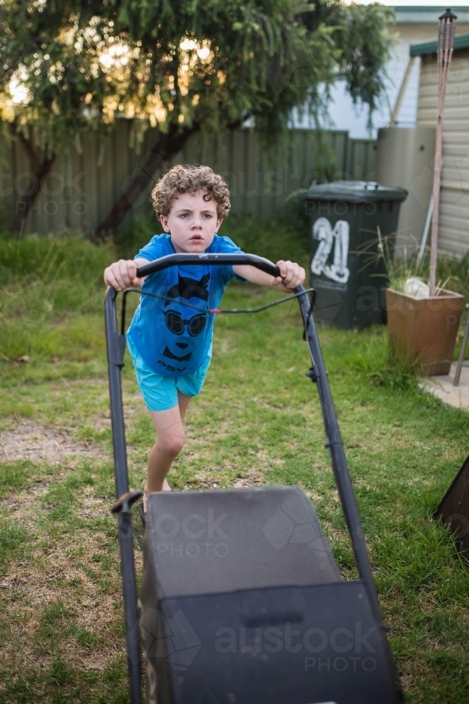 Boy pushing lawn mower mowing lawn - Australian Stock Image