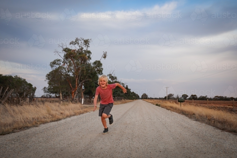 Boy running on dirt country road - Australian Stock Image