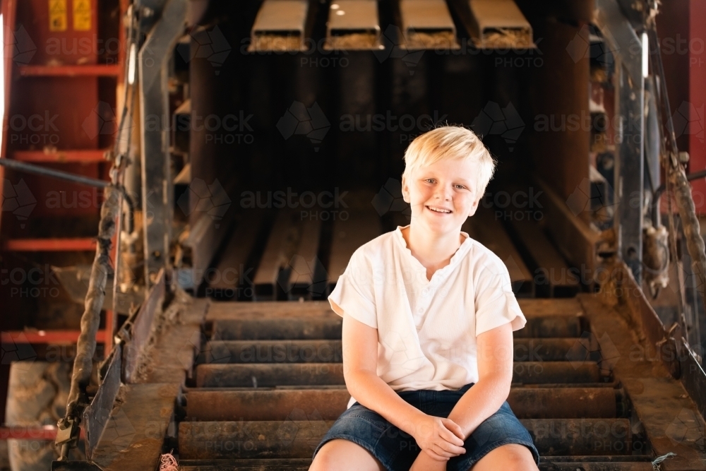 Boy sitting on farm machinery in country shed - Australian Stock Image