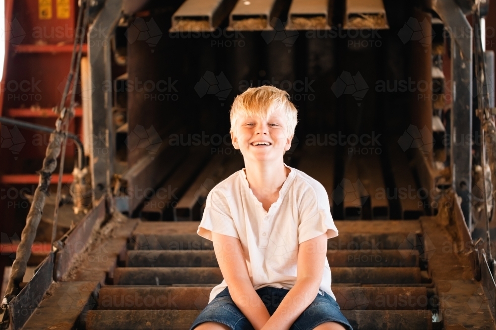 Boy sitting on farm machinery in country shed - Australian Stock Image